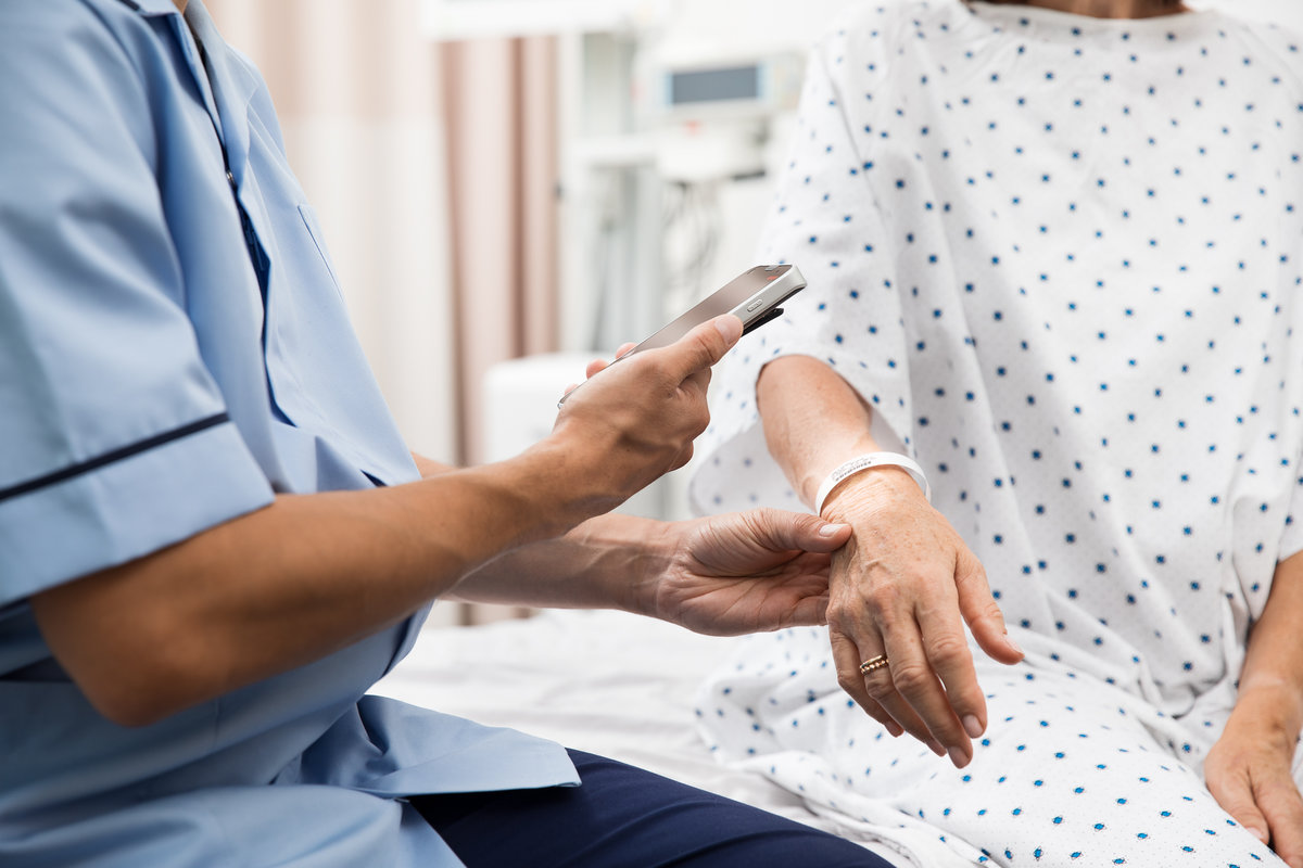 A nurse or medical worker scanning a patient's wristband identity, access or location tag.