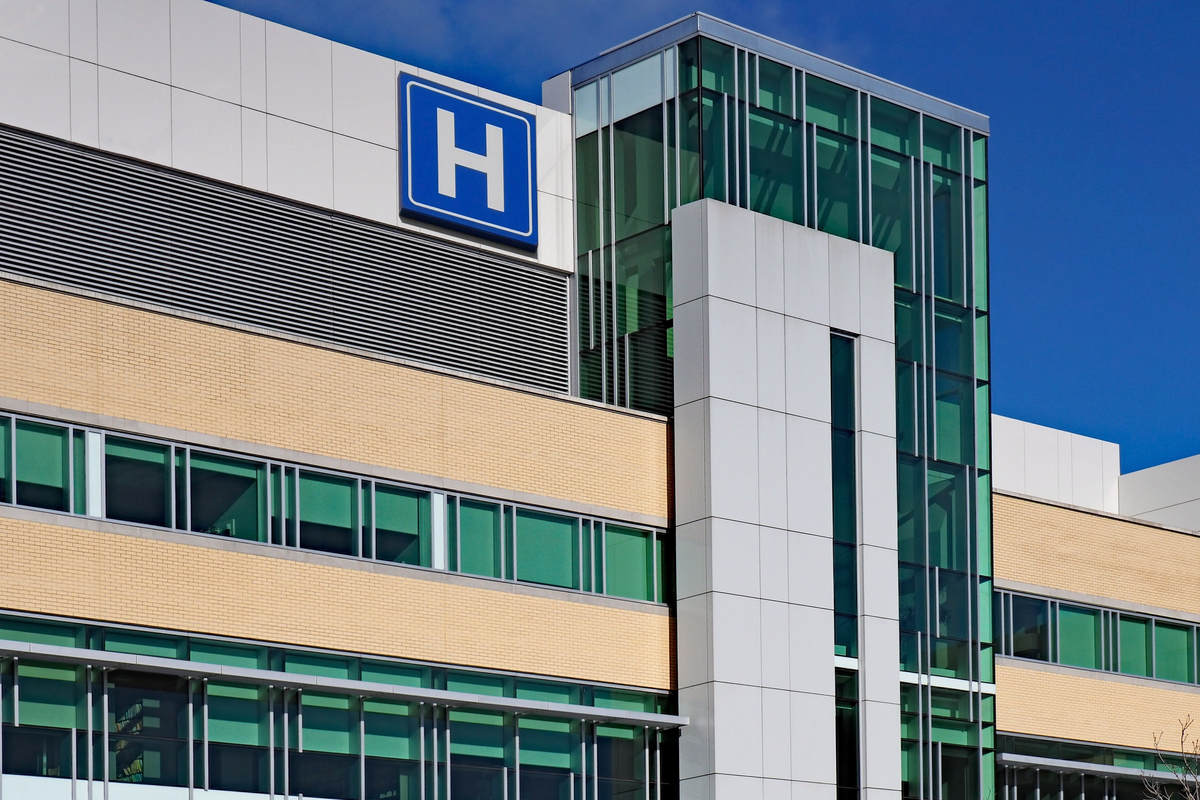 Hospital building, modern glass and steel with some brick, large rectangular hospital sign, white H on a big blue square, up top above the large a/c vents. A healthcare themed photo.