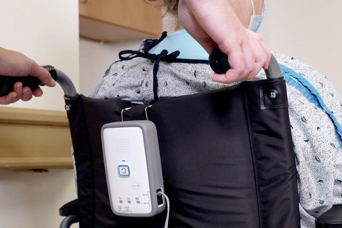 A Securitas Healthcare fall monitoring system device attached to a back of a patient's wheelchair.